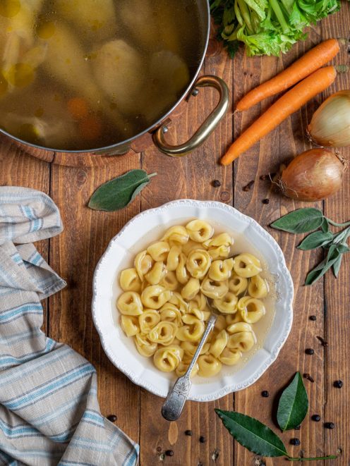 Tortellini in brodo serviti in un piatto fondo con brodo dorato e un cucchiaio
