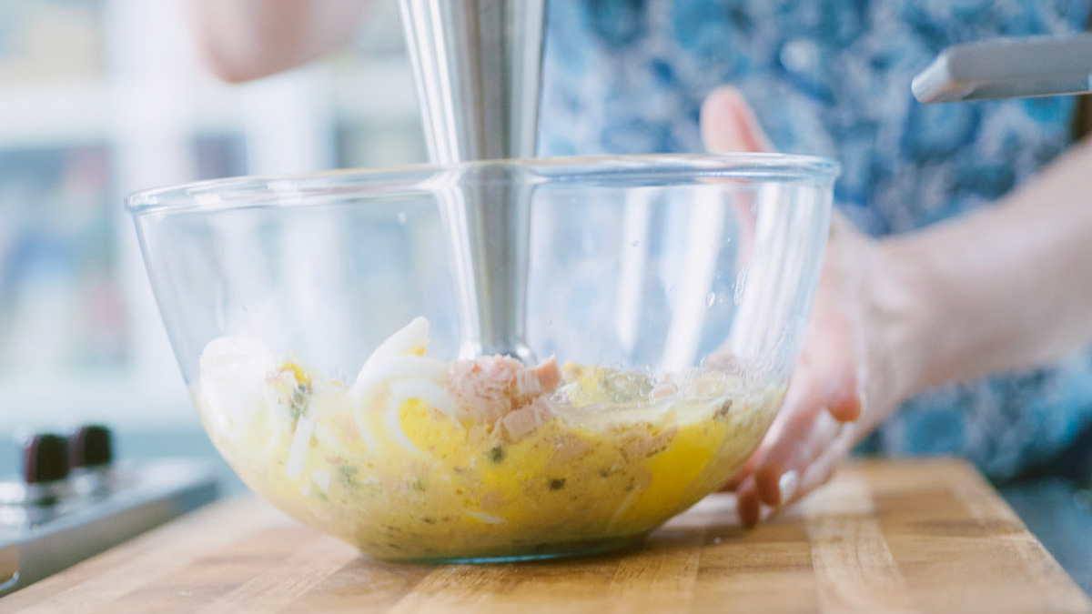 Frullatore a immersione immerso nella salsa tonnata con pezzi di tonno e uova ancora interi