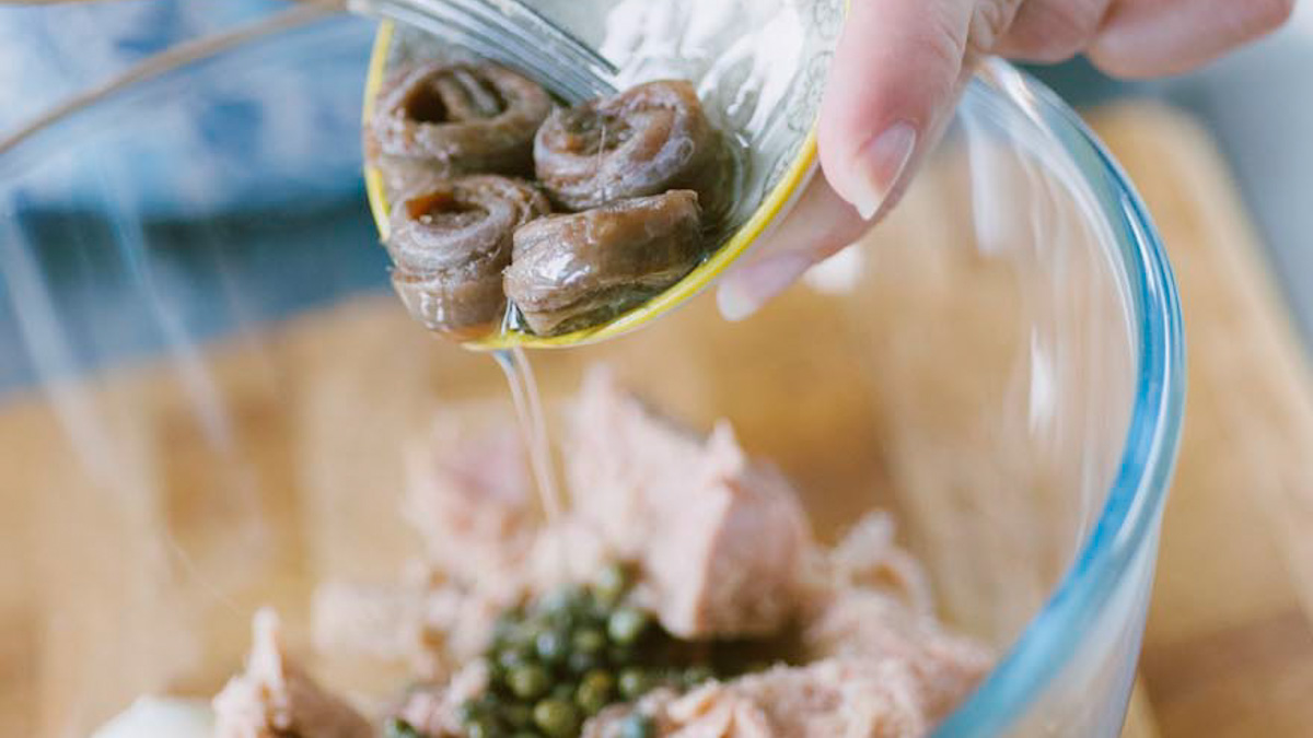 Acciughe arrotolate versate con il loro olio su tonno e capperi per la salsa tonnata