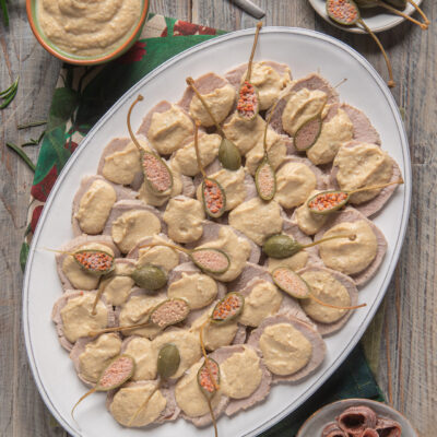 Vitello tonnato affettato con salsa al tonno e capperi interi disposti su vassoio ovale