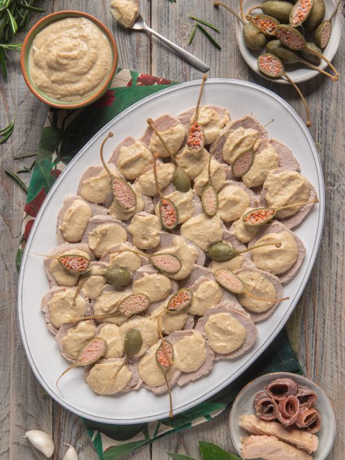 Vitello tonnato affettato con salsa al tonno e capperi interi disposti su vassoio ovale