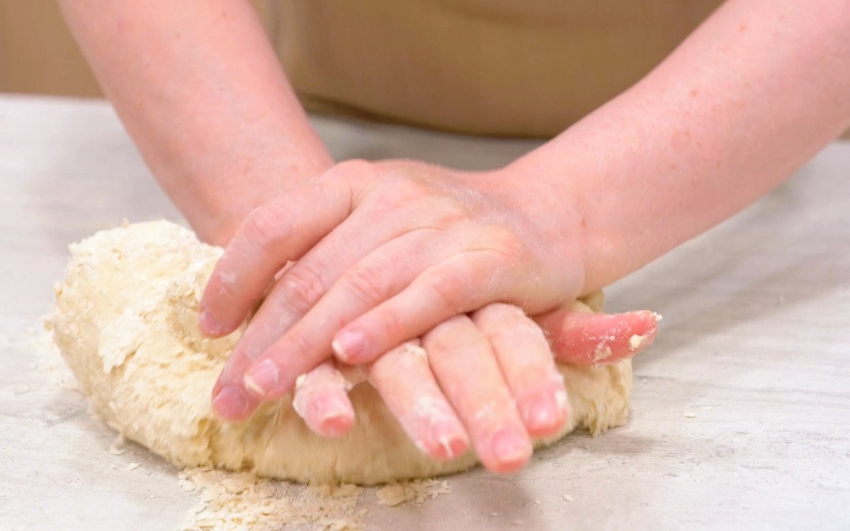 Mani che lavorano energicamente l'impasto della piadina sul piano infarinato