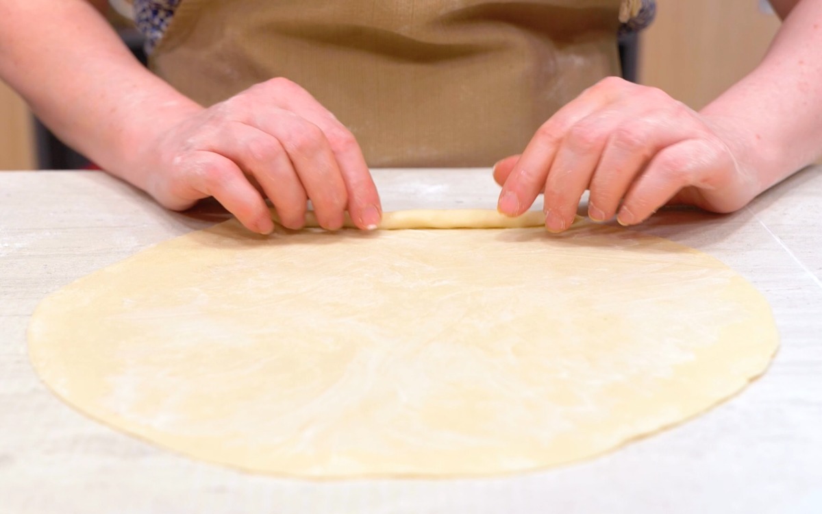 Mani che arrotolano un disco di impasto steso sul piano di lavoro