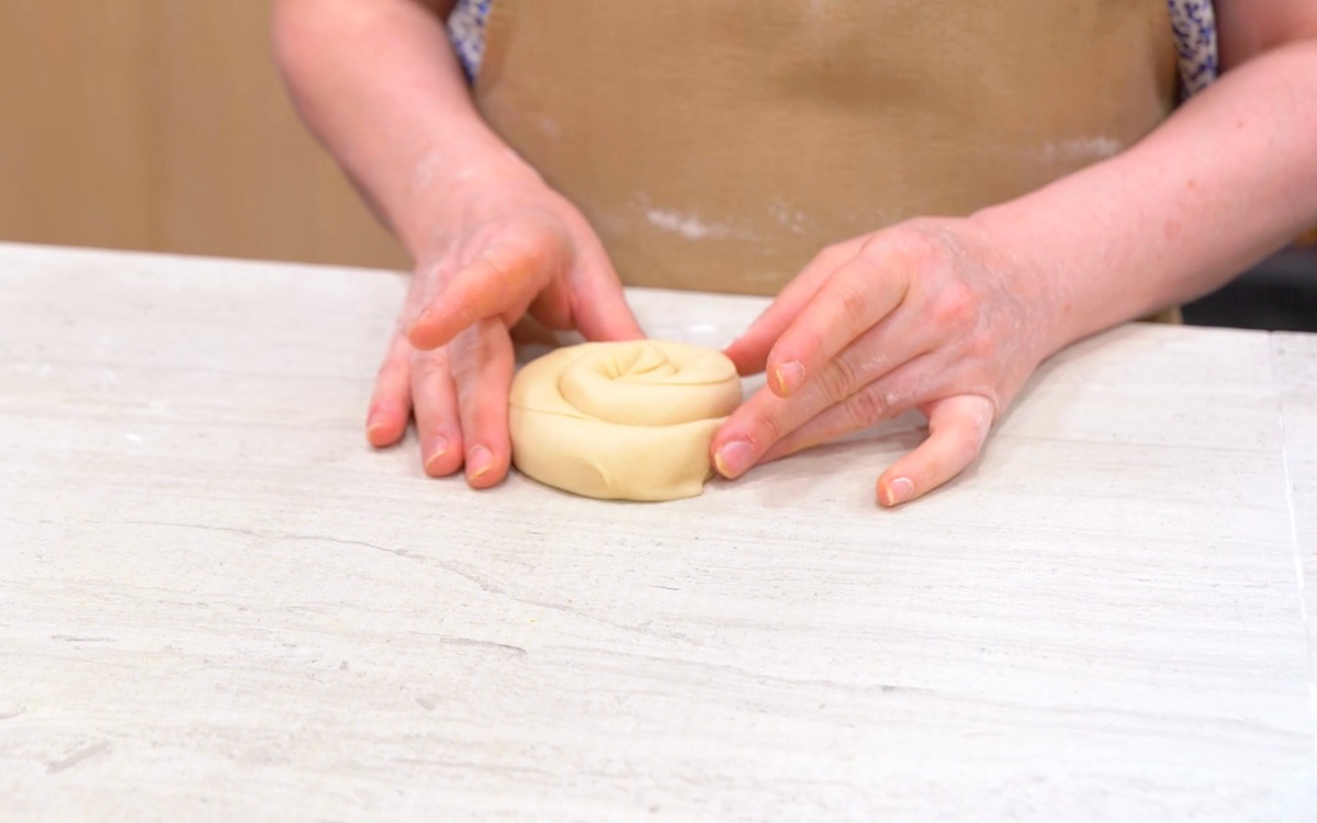 Mani che modellano un rotolo di pasta sfogliata a chiocciola sul piano di lavoro