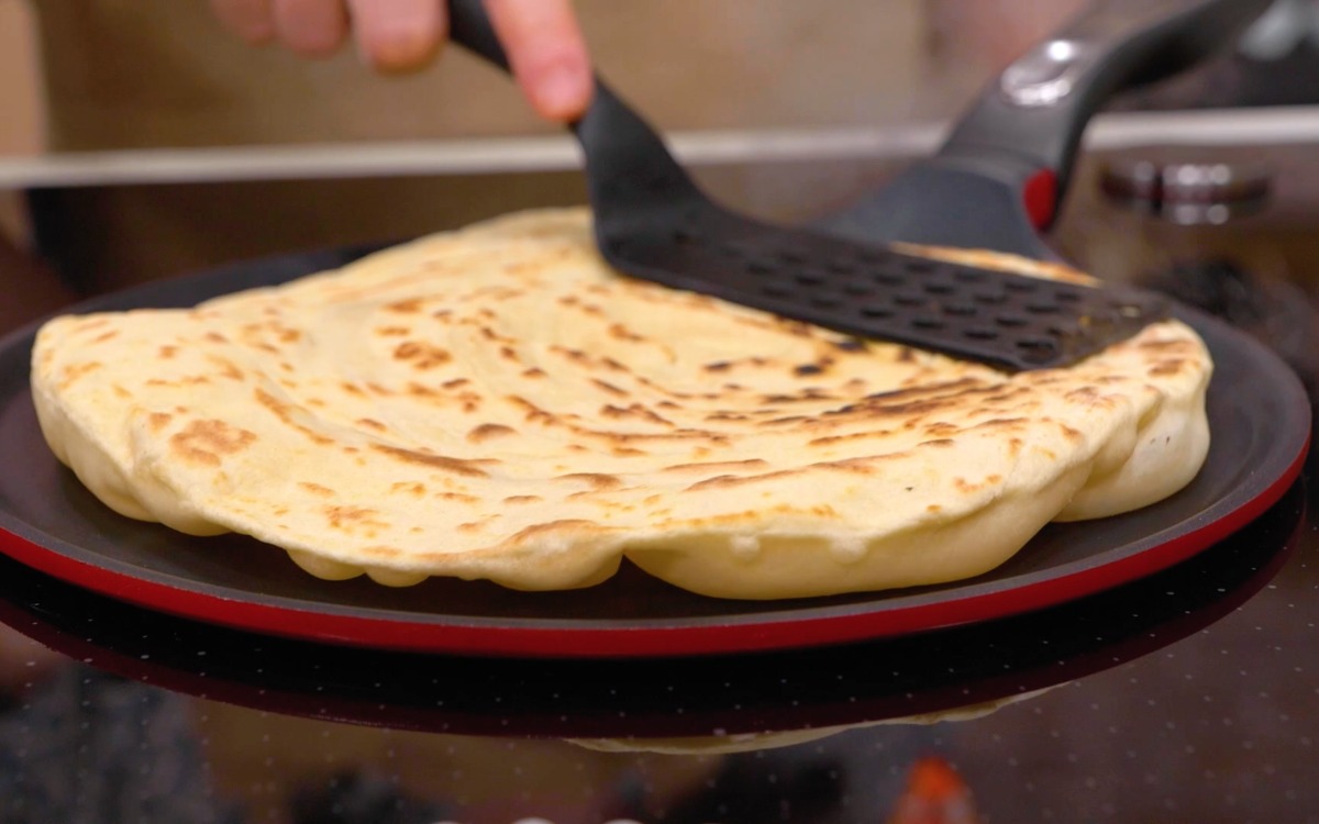 Piadina romagnola in cottura girata con la spatola, con macchie dorate ben visibili