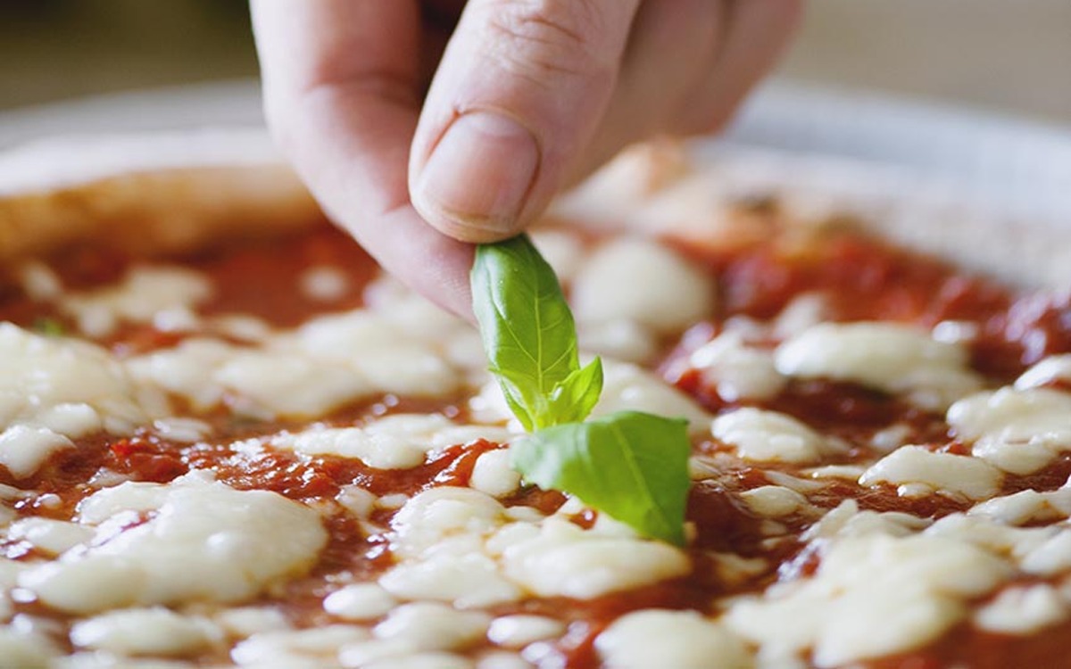 Una mano adagia una foglia di basilico fresco sulla pizza margherita condita con pomodoro e fiordilatte