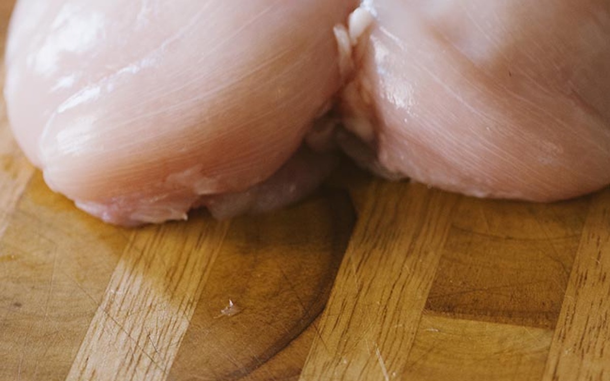 Due petti di pollo crudi interi sul tagliere, pronti per essere tagliati a cubetti
