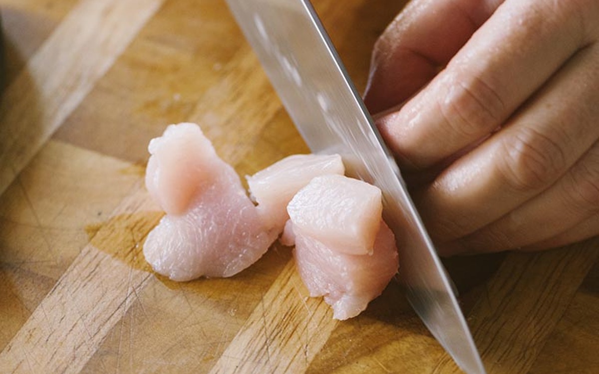 Petto di pollo crudo tagliato a cubetti con un coltello sul tagliere