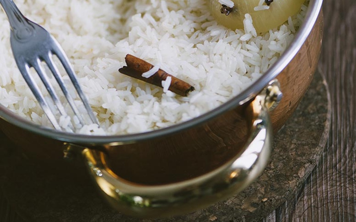Riso pilaf sgranato con una forchetta: si vedono una stecca di cannella e un'cipolla intera tra i chicchi