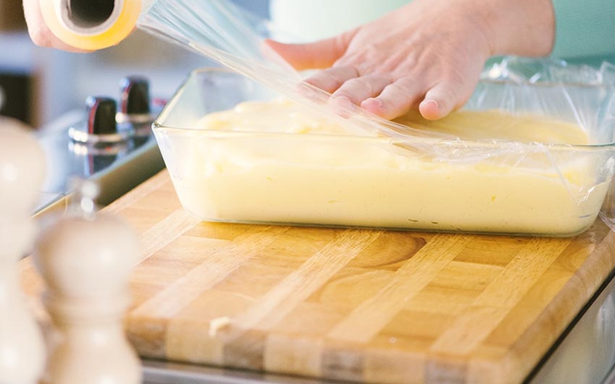 Crema pasticcera versata in una teglia e coperta con pellicola a contatto per raffreddarsi