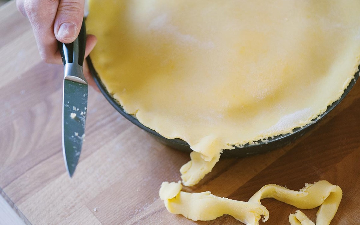 Mano che rifila con un coltello la pasta frolla in eccesso dal bordo dello stampo