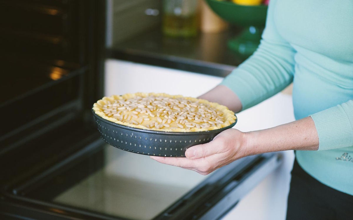 Mani che portano in forno la torta della nonna cruda, con pinoli sparsi sulla superficie