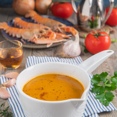Bisque di gamberi densa e aromatica, con scampi freschi, pomodori e aglio sullo sfondo