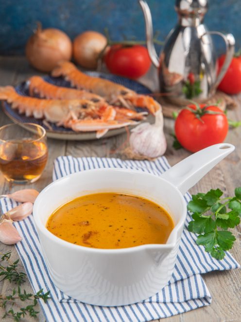 Bisque di gamberi densa e aromatica, con scampi freschi, pomodori e aglio sullo sfondo