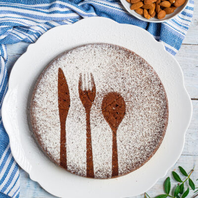 Torta caprese al cioccolato spolverata di zucchero a velo con decorazione a sagome di posate