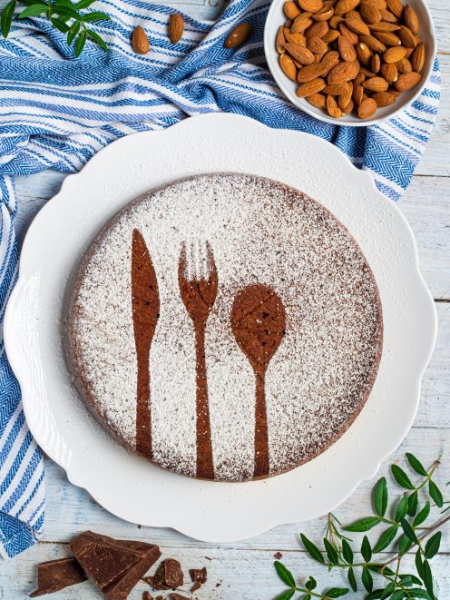 Torta caprese al cioccolato spolverata di zucchero a velo con decorazione a sagome di posate