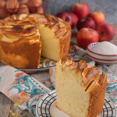 Fetta di chiffon cake alle mele soffice e alta, con fettine caramellate in superficie, torta intera sullo sfondo