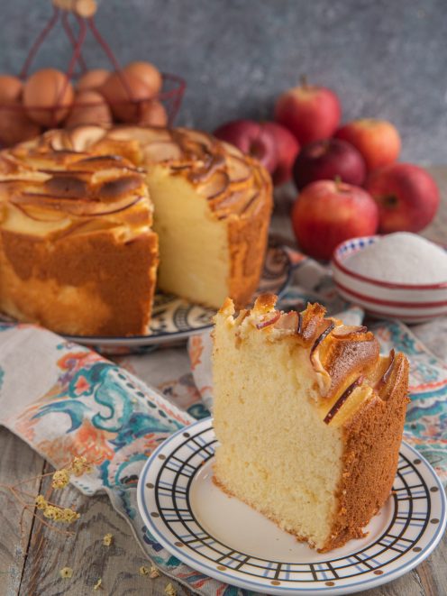 Fetta di chiffon cake alle mele soffice e alta, con fettine caramellate in superficie, torta intera sullo sfondo
