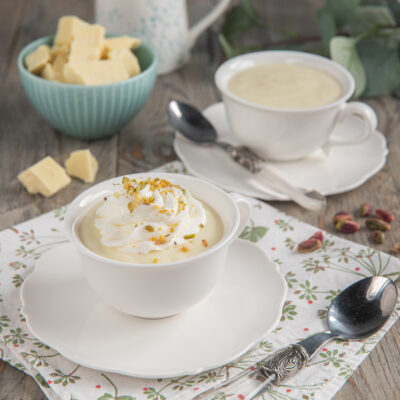 Cioccolata calda bianca in tazza con ciuffo di panna montata e granella di pistacchi
