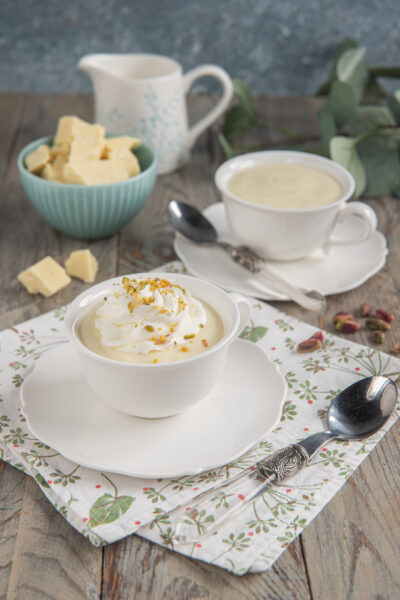 Cioccolata calda bianca in tazza con ciuffo di panna montata e granella di pistacchi