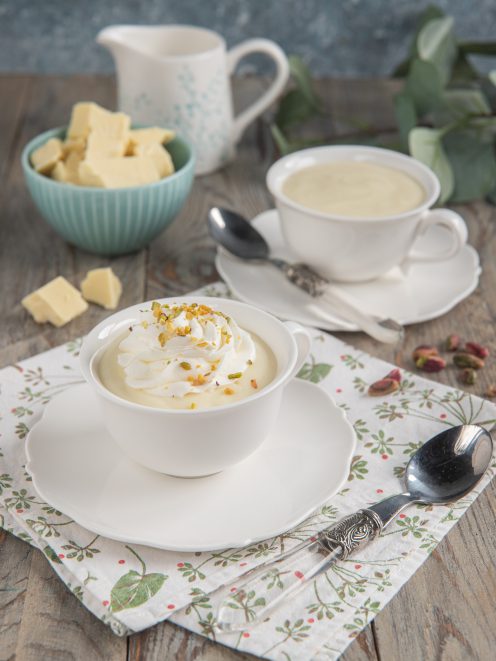Cioccolata calda bianca in tazza con ciuffo di panna montata e granella di pistacchi