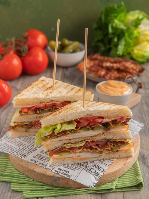 Club sandwich tagliato a triangoli con bacon, pomodoro, lattuga e salsa, fermato da stecchini