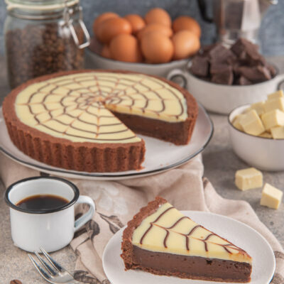 Crostata caffè e cioccolato bianco decorata a ragnatela, con una fetta servita accanto a una tazza di caffè