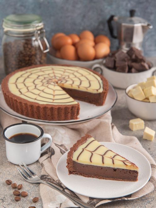 Crostata caffè e cioccolato bianco decorata a ragnatela, con una fetta servita accanto a una tazza di caffè