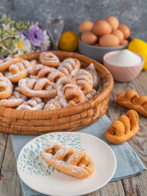 Nacatole calabresi fritte spolverizzate di zucchero a velo, servite in un cesto e su un piattino