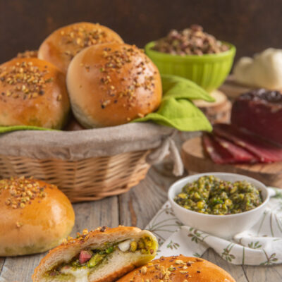 Panini ripieni con pesto di pistacchi, speck e mozzarella filante tagliati a meta e cosparsi di granella