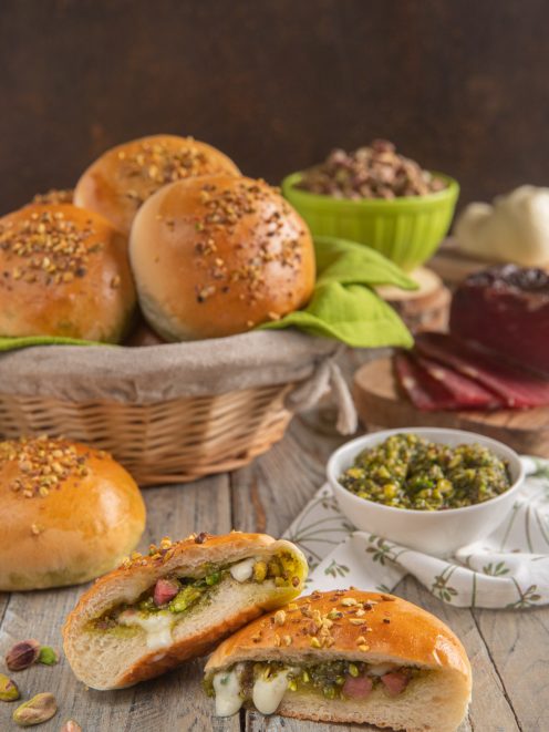 Panini ripieni con pesto di pistacchi, speck e mozzarella filante tagliati a meta e cosparsi di granella
