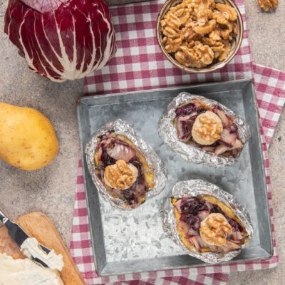 Patate al cartoccio ripiene di radicchio, gorgonzola e noci servite aperte su teglia