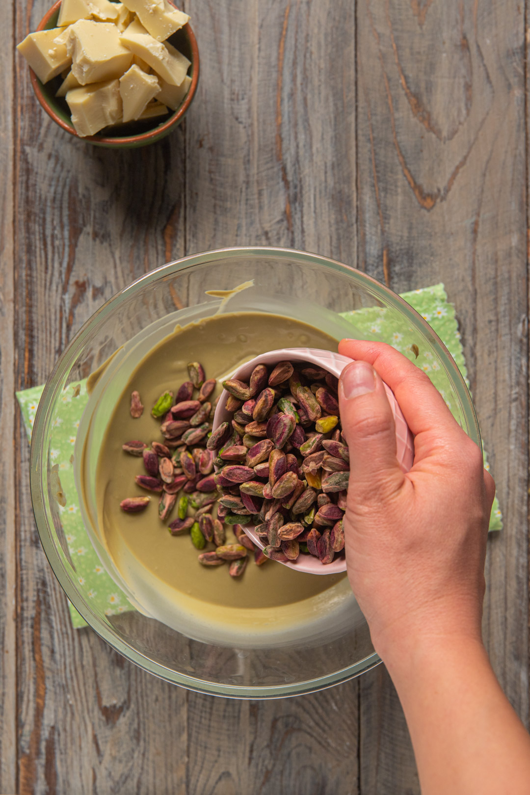 Pistacchi interi versati a mano nella crema al pistacchio fusa, in una ciotola di vetro