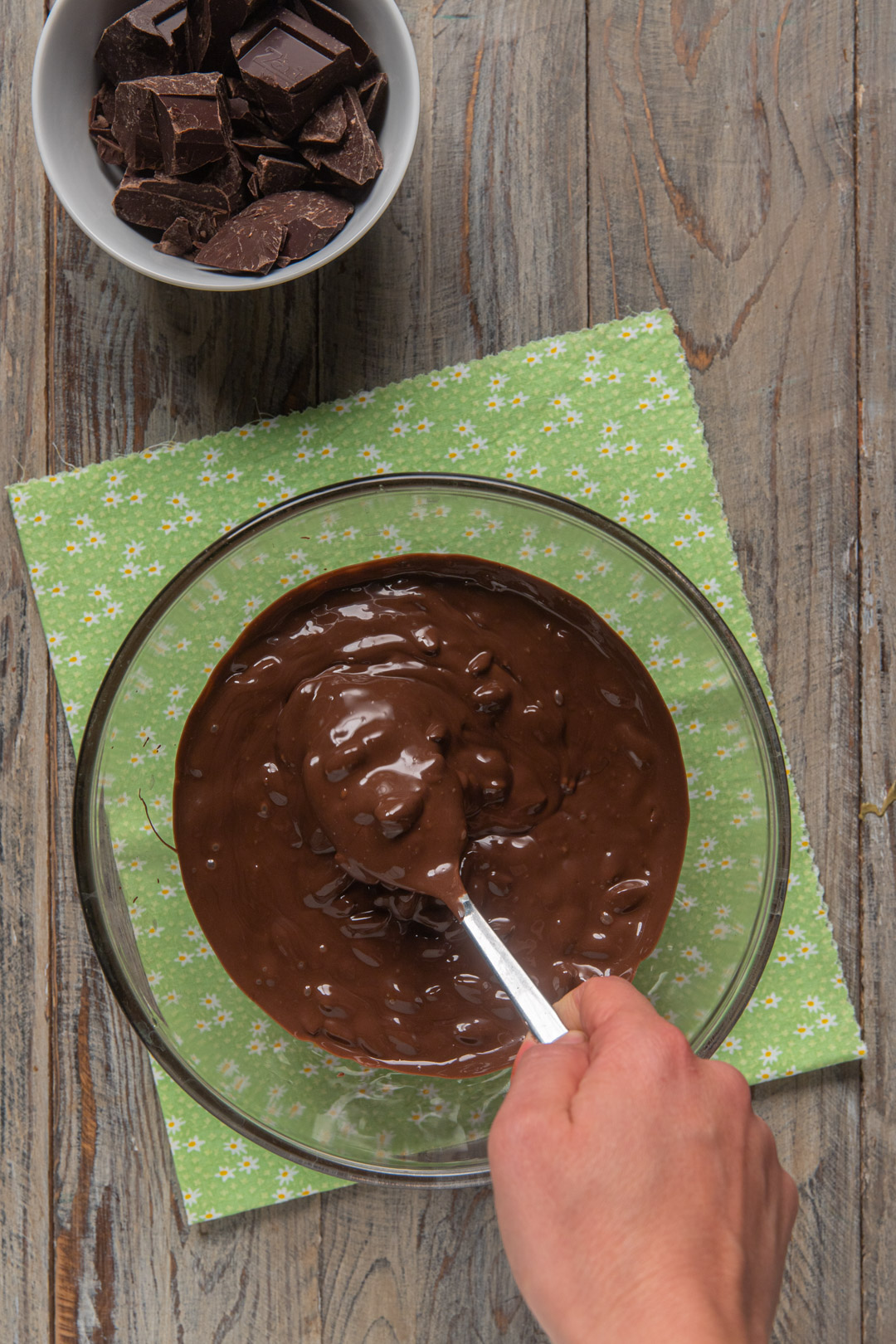 Mano che mescola con un cucchiaio il cioccolato fondente fuso in una ciotola di vetro