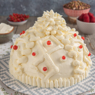 Torta berretto ricoperta di crema al pistacchio decorata con ribes rossi e ciuffi di panna a rilievo