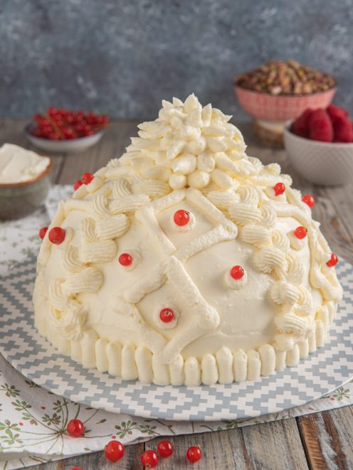 Torta berretto ricoperta di crema al pistacchio decorata con ribes rossi e ciuffi di panna a rilievo