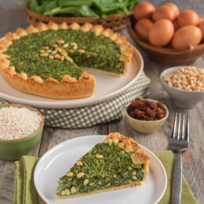 Torta coi becchi con ripieno di spinaci e pinoli, una fetta tagliata servita in primo piano