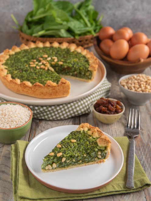 Torta coi becchi con ripieno di spinaci e pinoli, una fetta tagliata servita in primo piano