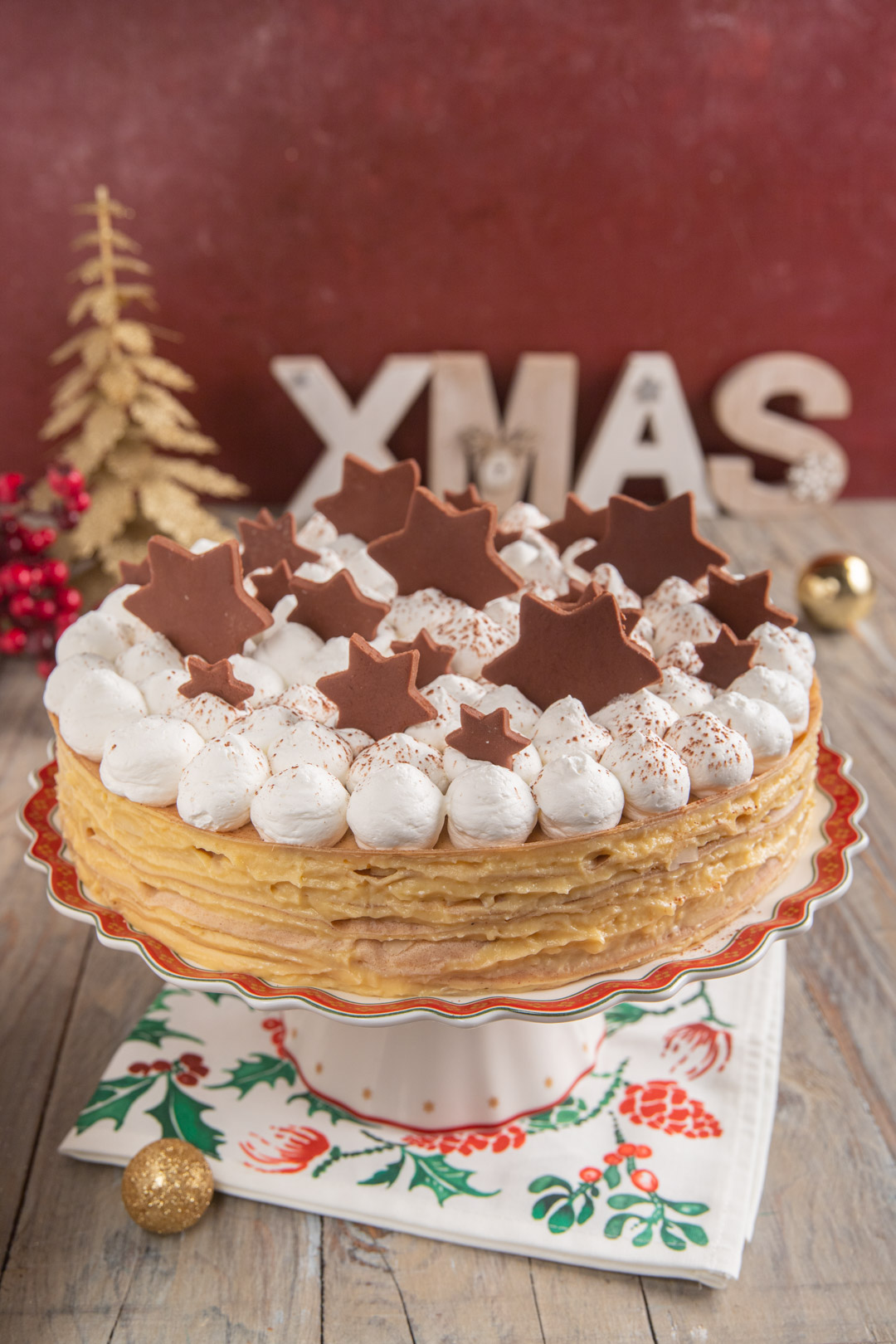 Torta di crepes decorata con ciuffi di meringa, stelle di cioccolato e cacao spolverato