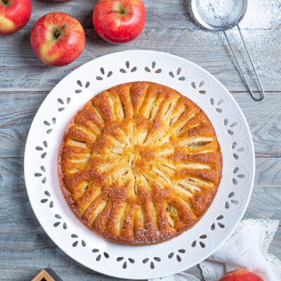 Torta di mele dorata con fettine di mela disposte a raggiera e zucchero a velo