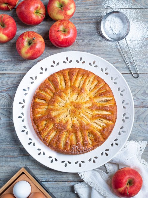 Torta di mele dorata con fettine di mela disposte a raggiera e zucchero a velo
