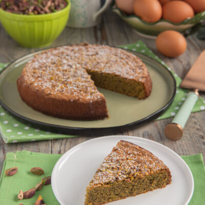 Torta tenerina al pistacchio con una fetta servita, spolverata di zucchero a velo e granella
