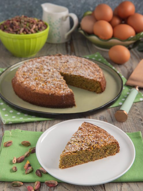 Torta tenerina al pistacchio con una fetta servita, spolverata di zucchero a velo e granella