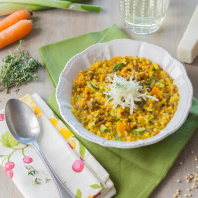 Fregola con zucchine, salsiccia e zafferano in ciotola, guarnita con julienne di sedano rapa