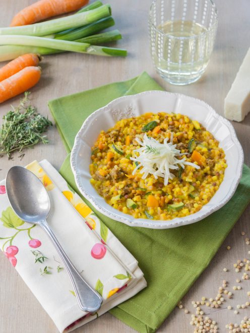 Fregola con zucchine, salsiccia e zafferano in ciotola, guarnita con julienne di sedano rapa