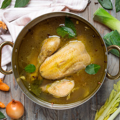 Brodo di pollo con pezzi di carne, foglie di alloro e grani di pepe in cottura