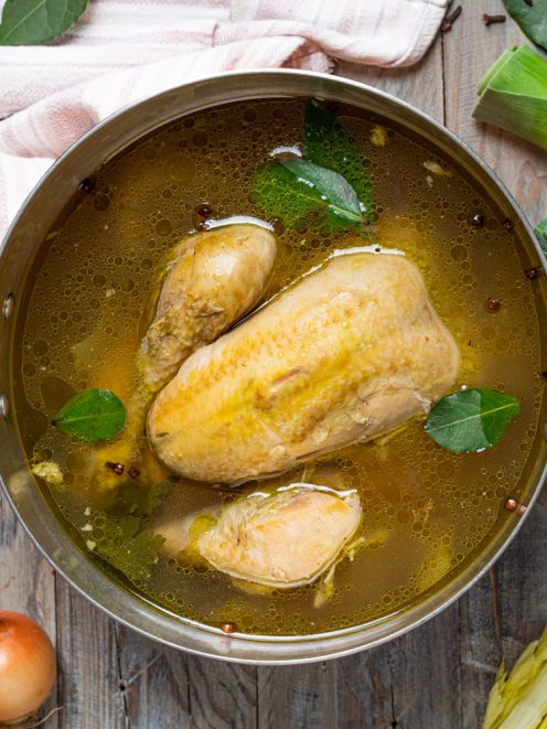 Brodo di pollo con pezzi di carne, foglie di alloro e grani di pepe in cottura