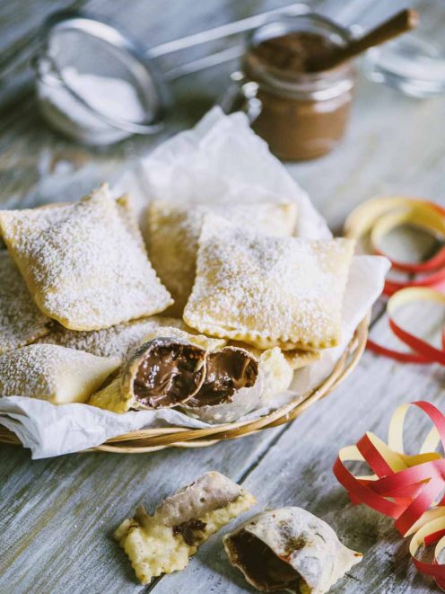 Bugie ripiene di cioccolato spolverate di zucchero a velo, aperte a mostrare il cuore morbido
