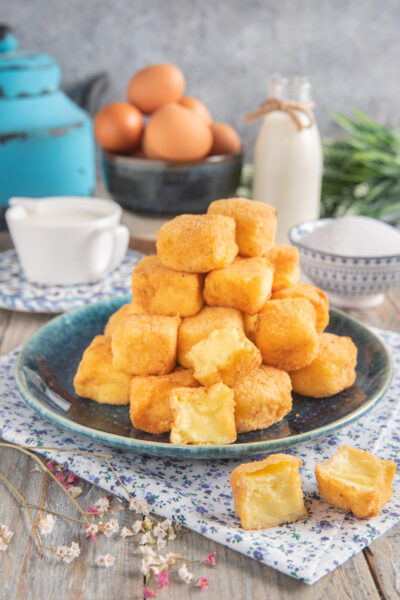 Crema fritta impilata a piramide, con uno spezzato che mostra il cuore morbido di crema pasticcera