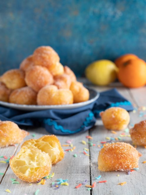 Frittelle di Carnevale fritte e zuccherate, una spezzata mostra l'interno soffice e alveolato